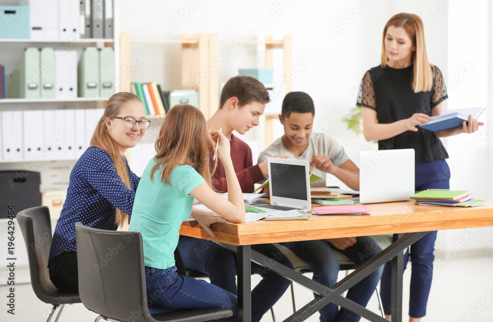 Obraz premium Group of teenagers doing homework with teacher in classroom