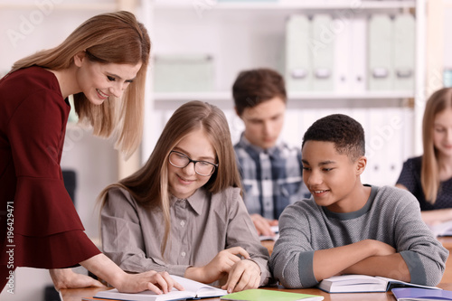 Group of teenagers doing homework with teacher in classroom