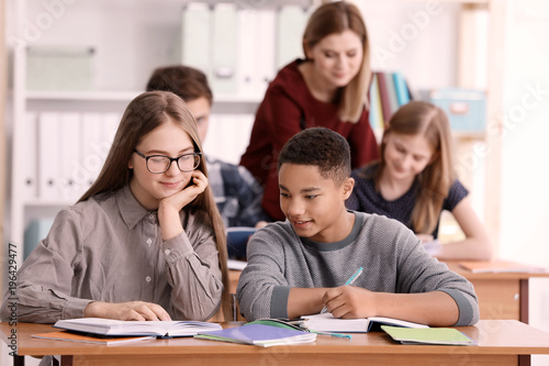 Group of teenagers doing homework with teacher in classroom
