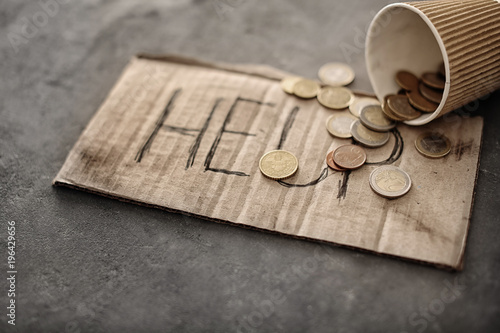 Piece of cardboard with word HELP and coins on grey background. Poverty concept
