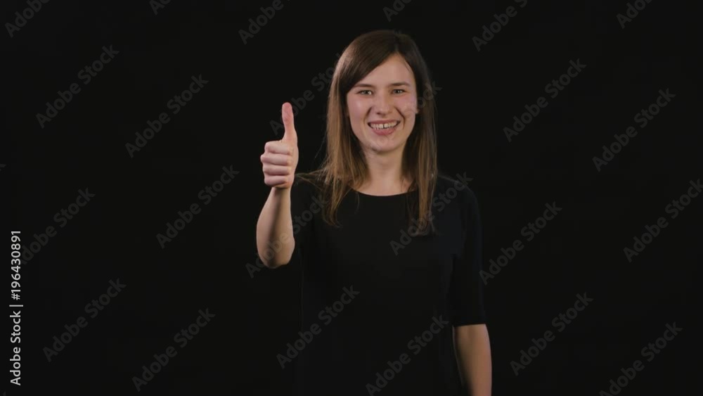 A beautiful young lady showing a Thumbs Up gesture against a black background. Medium Shot A beautiful young lady showing a Thumbs Up gesture against a black background. Medium Shot