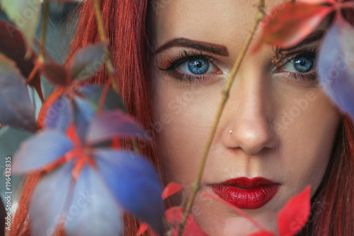 Close up of a beautiful red head woman among the colorful autumn leaves