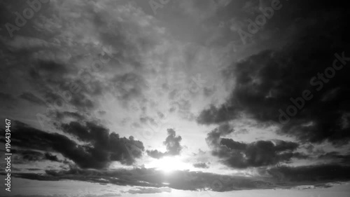 Timelapse of a cloudscape in black and white with dark clouds passing in front of the sun in late evening, before sunset. Cumulus and stratocumulus in a sky becoming clearer, showing a low sun.
