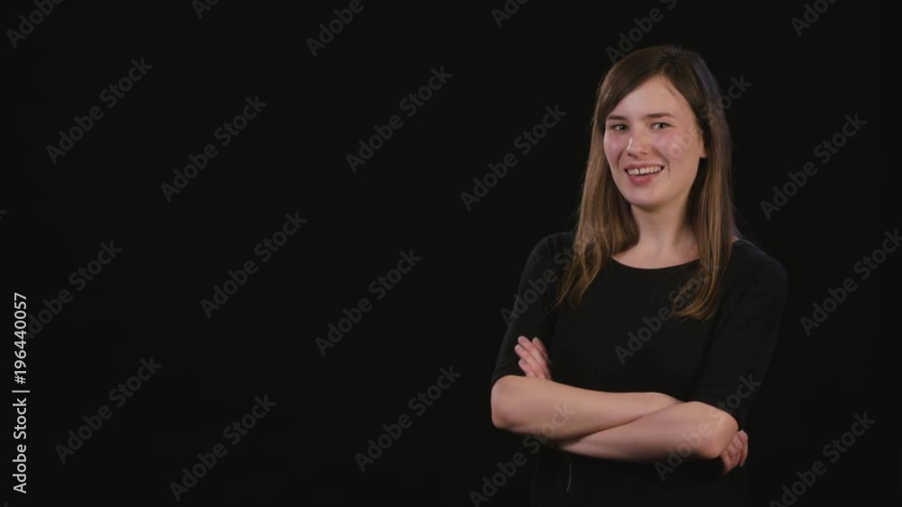 A beautiful young lady smiling and standing with her arms folded against a black background. Medium Shot A beautiful young lady smiling and standing with her arms folded against a black background. Medium Shot