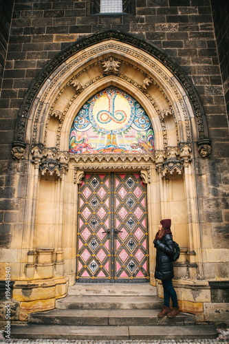 The tourists girl stands next to the beautiful antique door to the Catholic cathedral located in the High City called Vysehrad in Prague. Entrance to the cathedral. Exterior of a religious building. photo