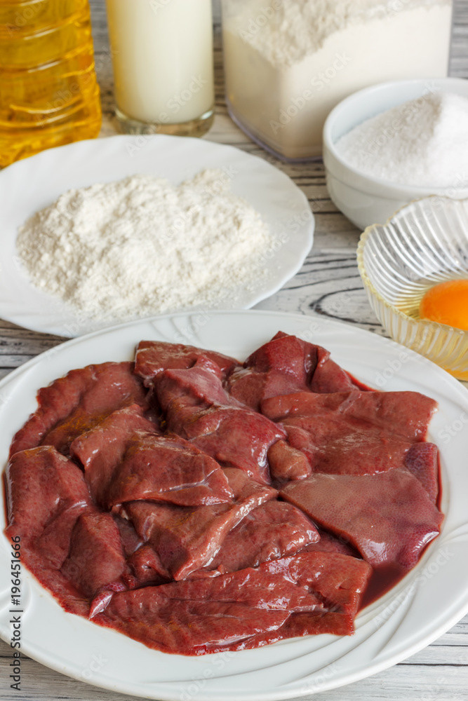 Raw liver on a white plate on a wooden background. A set of products for cooking fried liver egg oil salt flour. Food ingredient. Selective focus.