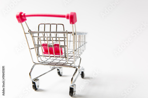 Close up of supermarket grocery push cart for shopping with black wheels and pink plastic elements on handle isolated on white background. Concept of shopping. Copy space for advertisement