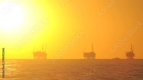Day to night time lapse of the sun setting behind three oil platforms in the Santa Barbara Channel, California.