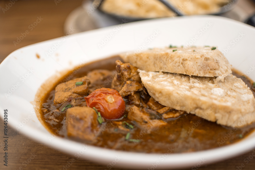 Traditional Goulash with knedle in a white bowl of beef stew on the wooden table, Germany menu Traditional Goulash with knedle in a white bowl of beef stew on the wooden table, Germany menu