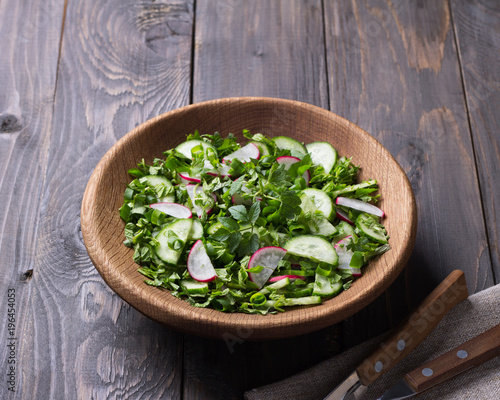 Vitamin salad of wild herbs with cucumber, radish and green onions in a wooden bowl on a wooden background. Healthy detox diet food