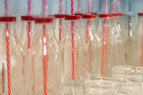 Empty glass bottles for water, liquid food, smoothies with red lids with holes for tubes and with red striped tubes. Close up, blured background