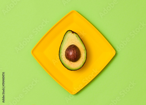 Avocado Tropical Fresh Fruit. Vegan Organic Food Concept. Flat lay. Trendy fashion Style. Minimal Design Art. Hot Summer Vibes. Green avocado on yellow plate. Bright Color.