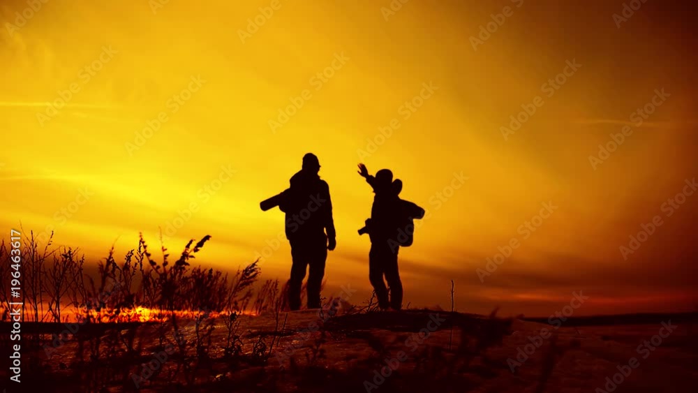 Silhouettes of two hikers with backpacks enjoying sunset view from top of a mountain Silhouettes of two hikers with backpacks enjoying sunset view from top of a mountain