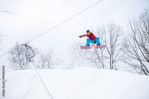 Image of sportive male snowboarder jumping on snowy hill