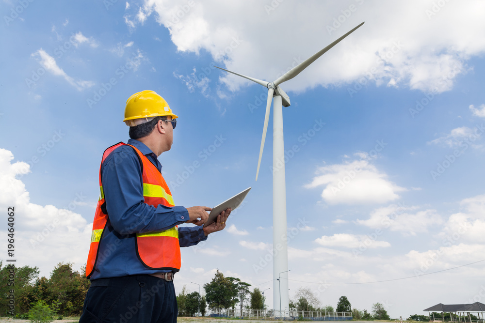Electric Engineer use Tablet Device with Wind turbine power Generator Tower