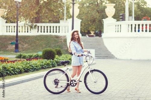 Pretty smiling girl in dress with retro bicycle on a city street and looking at camera