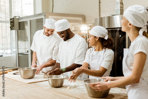 group of happy multiethnic bakers kneading dough together