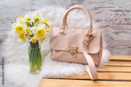 Pink hahdbag and bouquet of daffodils on white fur. Fashionable concept photo