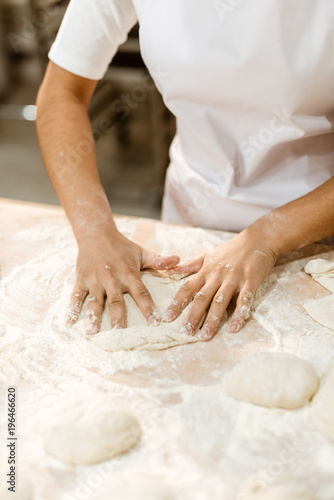 cropped shot of female baker kneading dough for pastry on messy table