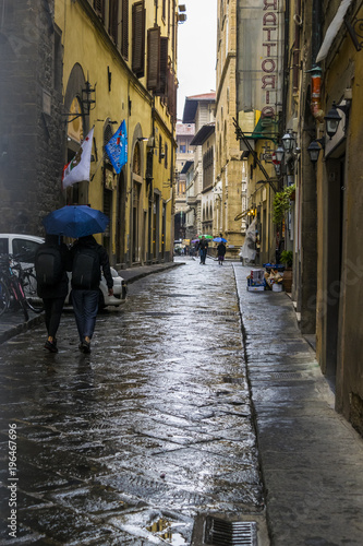 Street detail of the historic Florence  Italy.  Tourists are walking with umbrellas in the rainy weather. 