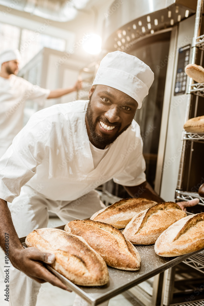 happy african american baker taking bread loaves from oven at baking manufacture happy african american baker taking bread loaves from oven at baking manufacture