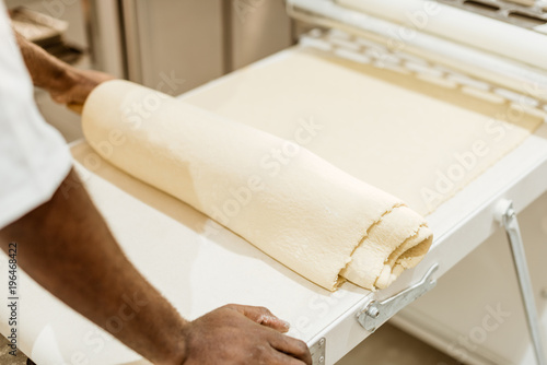 cropped shot of african american baker with roll of raw dough on baking manufacture