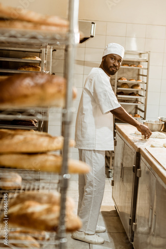african american baker preparing raw dough at workplace on baking manufacture