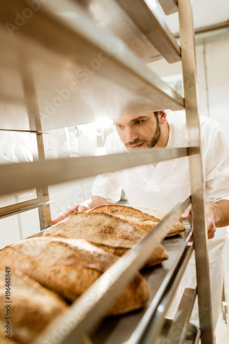 close-up shot of baker putting trays of fresh bread on stand at baking manufacture