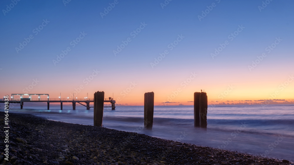 A pier on a rocky beach, sunset background