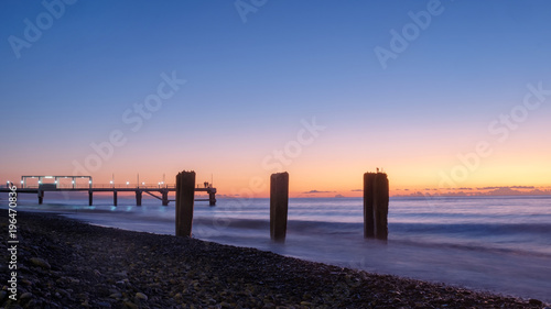 A pier on a rocky beach, sunset background © Luka