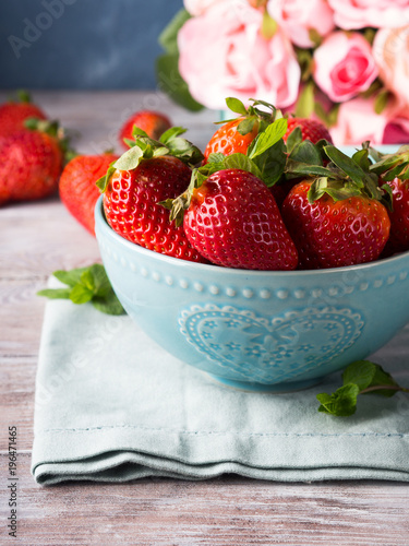 Fresh spring strawberries in blue bowl with heart and pink roses in the background