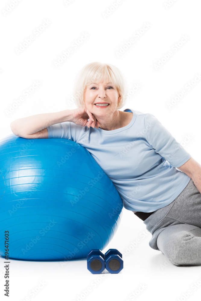 Smiling senior sportswoman with fitness ball and dumbbells isolated on white Smiling senior sportswoman with fitness ball and dumbbells isolated on white