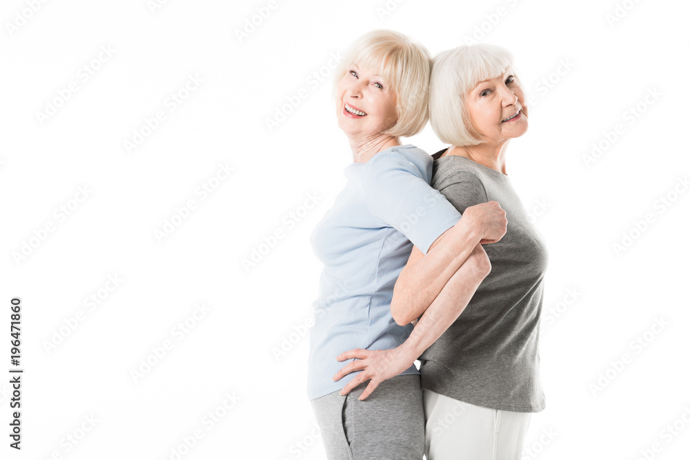 Two senior sportswomen standing back to back while doing excercise isolated on white Two senior sportswomen standing back to back while doing excercise isolated on white