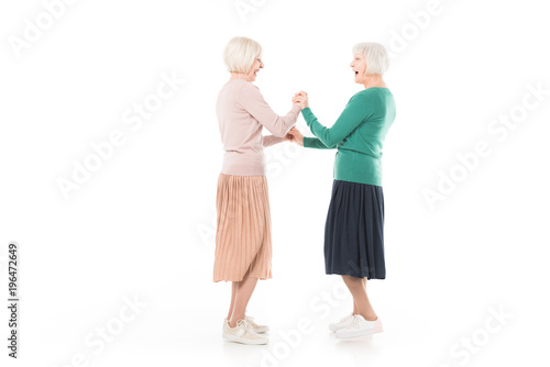 Side view of two senior stylish women holding hands of each other isolated on white