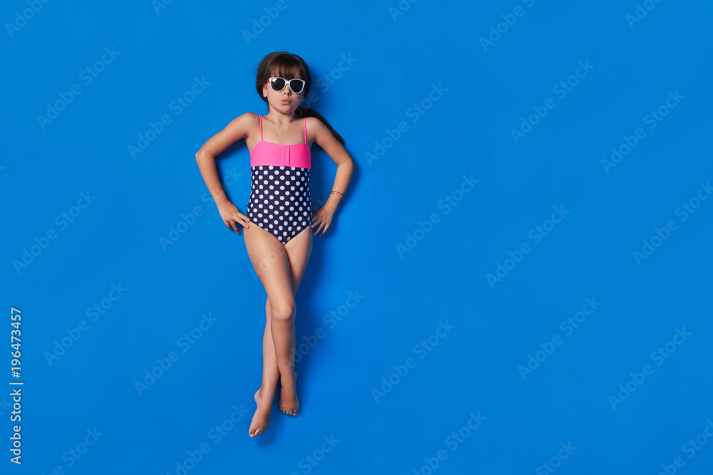 Child bikini view top.Little stylish lady girl in swimsuit,relaxing isolated blue background.Lovely photo for advertising,copy space for text.Beach Vacation concept.Kid model lay full-length. Child bikini view top.Little stylish lady girl in swimsuit,relaxing isolated blue background.Lovely photo for advertising,copy space for text.Beach Vacation concept.Kid model lay full-length.