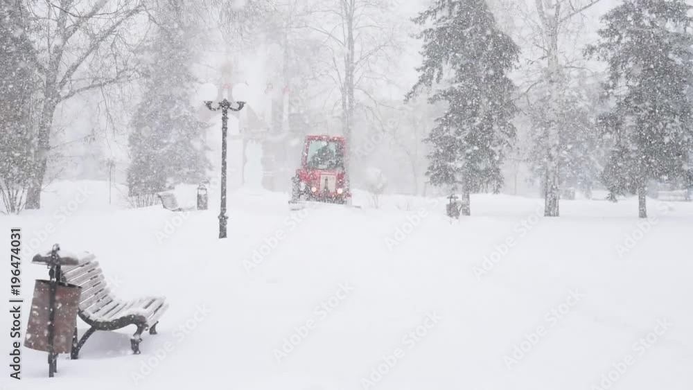 Red tractor cleans the road from the snow in the park Red tractor cleans the road from the snow in the park