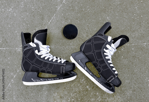 Pair of hockey skates with puck on a ice rink.