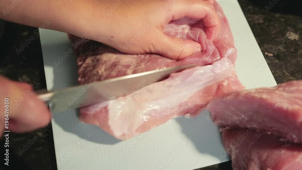 woman with knife in hand cuts fresh meat on plastic cutting Board in home kitchen woman with knife in hand cuts fresh meat on plastic cutting Board in home kitchen