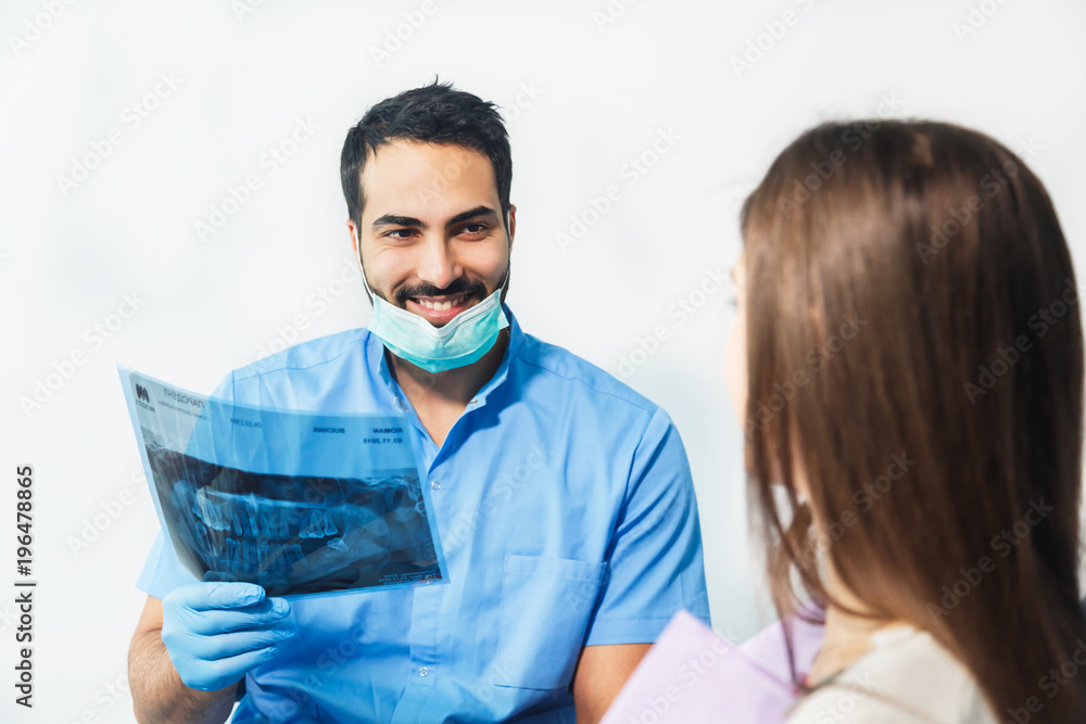 Dentist using x-ray during dental treatment, pointing at the teeth scan and explaining the problem, pretty woman in white top sitting in dental chair at the doctor's Dentist using x-ray during dental treatment, pointing at the teeth scan and explaining the problem, pretty woman in white top sitting in dental chair at the doctor's