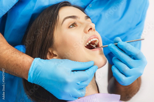 Dentist examining patient's teeth, looking at patient's teeth carefully with dental instruments, long-haired girl opening the mouth