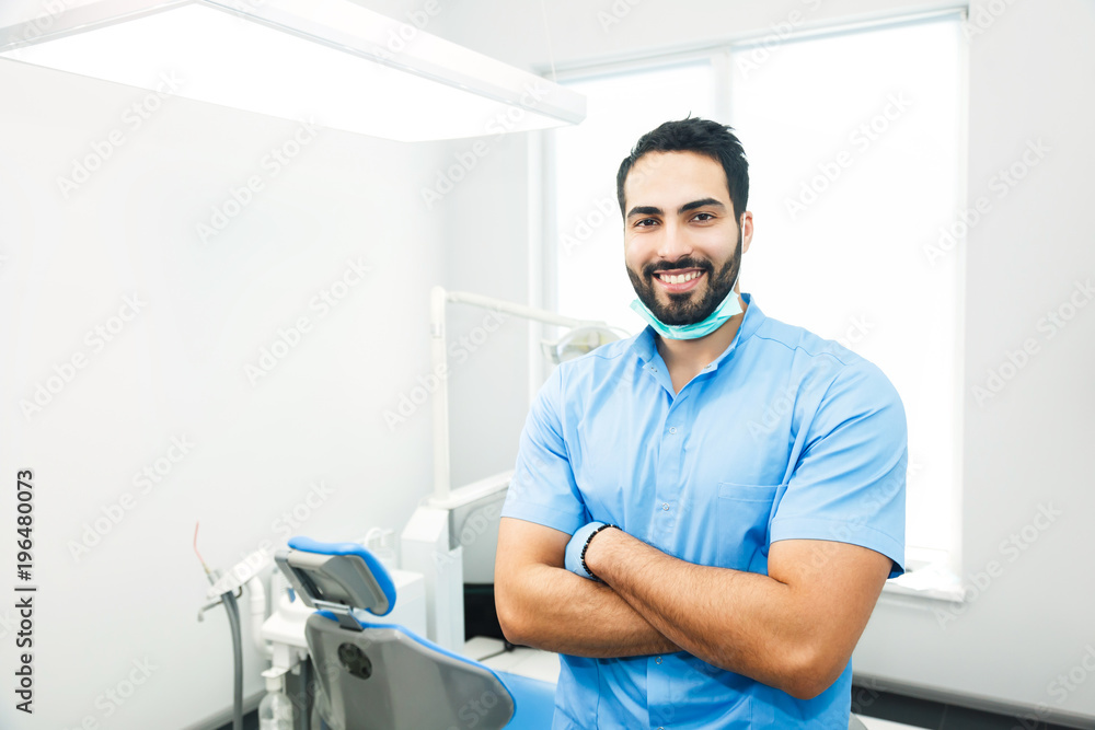 Obraz premium Portrait of hadsome dentist doctor wears blue uniform, indoor shot in modern dentist office
