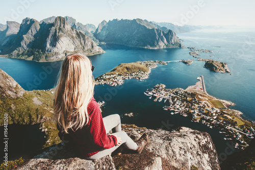 Blonde woman relaxing on cliff mountain top traveling in Norway lifestyle exploring concept adventure outdoor summer vacations Reinebringen aerial view Lofoten islands photo
