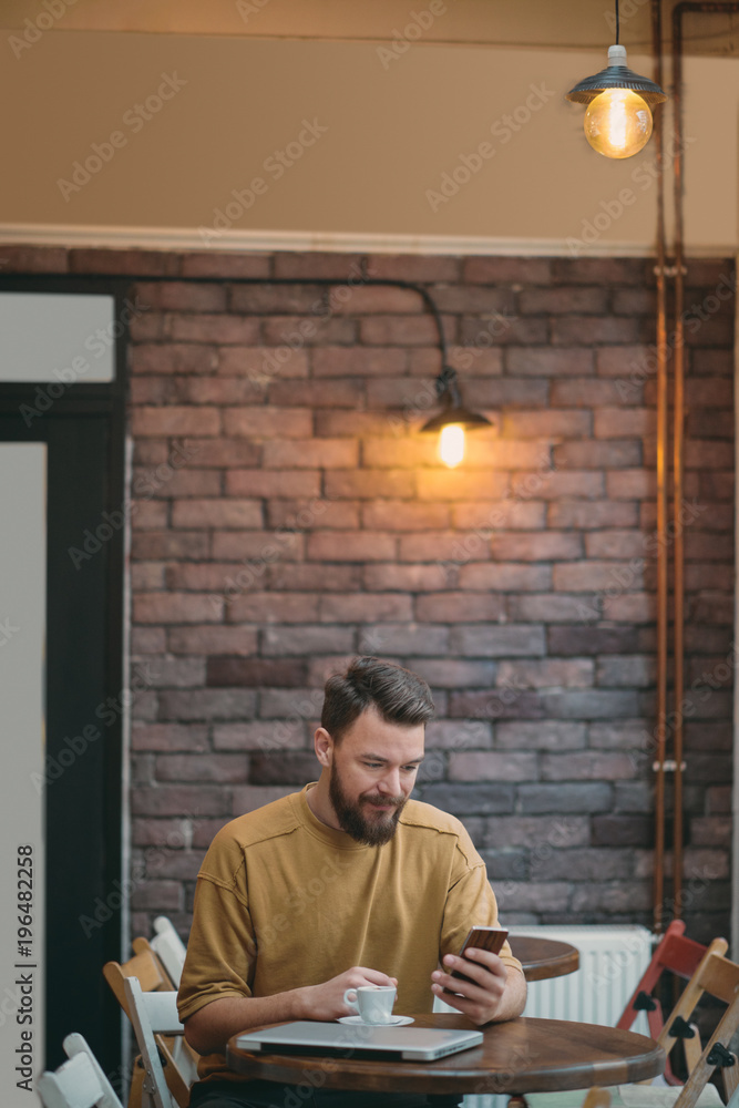 Fototapeta premium Young man sitting in cafe and using smart phone.