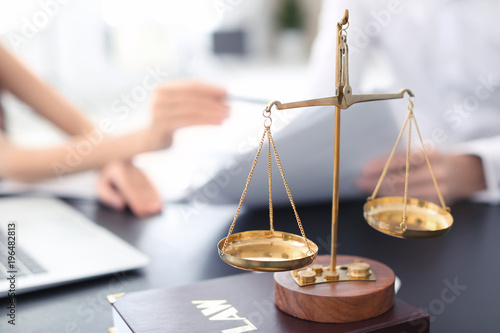 Scales of justice with juridical book on table in lawyer's office