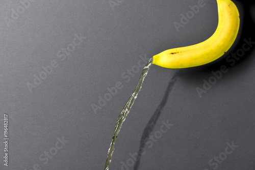 Banana on a dark background, from which a stream of liquid flows.