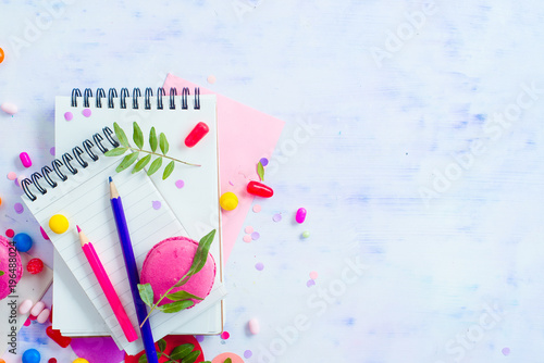 Blank lined notepads with colorful pencils, sweets and pink macaron cookie on a light background with copy space. Party planning fun concept.