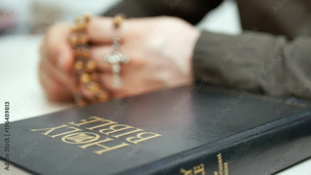 Man praying holds in hand wooden rosary with cross. Holy bible on the table. Sunday Bible reading in church Man praying holds in hand wooden rosary with cross. Holy bible on the table. Sunday Bible reading in church