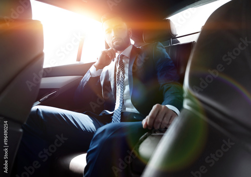 businessman talking on the phone while sitting in the back seat of his car