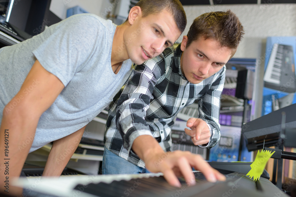 Young men looking at electronic keyboard Young men looking at electronic keyboard