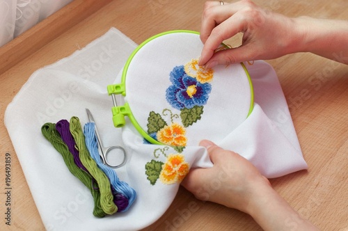 Female hands are embroidering flowers on the canvas. Cross stitch technique.